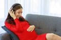 Caucasian millennial young happy sexy female prenatal pregnant mother in casual red pregnancy dress lay down on cozy sofa wearing Royalty Free Stock Photo