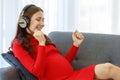 Caucasian millennial young happy sexy female prenatal pregnant mother in casual red pregnancy dress lay down on cozy sofa wearing Royalty Free Stock Photo