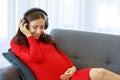 Caucasian millennial young happy sexy female prenatal pregnant mother in casual red pregnancy dress lay down on cozy sofa wearing Royalty Free Stock Photo