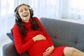 Caucasian millennial young happy sexy female prenatal pregnant mother in casual red pregnancy dress lay down on cozy sofa wearing Royalty Free Stock Photo