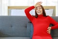 Caucasian millennial young happy sexy female prenatal pregnant mother in casual red pregnancy dress sitting on sofa holding hands Royalty Free Stock Photo