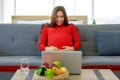 Caucasian millennial young happy sexy female prenatal pregnant mother in casual red pregnancy dress sitting on sofa holding hands Royalty Free Stock Photo