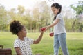 Caucasian mix girl handing apple to African girl at outdoors park, picnic time, Relationship little kids, Diverse black and white