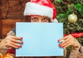 Caucasian Model Female in a Santa Hat Covered the Lower Part of her Face with a Bluish Sheet of Paper, has Pen in her Royalty Free Stock Photo