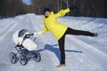 Caucasian mom in yellow coat is walking with white baby carriage on snow road among the forest at winter sunny day Royalty Free Stock Photo