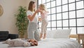 Caucasian mother and daughter bonding, jumping on the bed together, smiling inside their cozy bedroom, waking up a happy home with Royalty Free Stock Photo