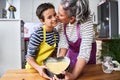 Caucasian mother with gray hair gives a kiss to her son showing the heart cake they have prepared to put in the oven