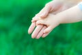 Caucasian mother holding hand of newborn baby on green grass background. The concept of maternal love, care and health. Royalty Free Stock Photo