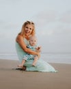 Caucasian mother holding infant baby boy, spending time on the beach. Sitting on the sand. Happy smiling mum with little son. Royalty Free Stock Photo