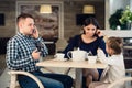 Caucasian mother and little child girl in restaurant while their busy father talking cellphone.