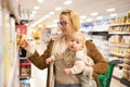 Caucasian mother shopping with her infant baby boy child choosing products in department of supermarket grocery store. Royalty Free Stock Photo