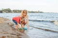 Caucasian Mother With Toddler Son Child Putting Paper Boats In Water Together On Lake Shore.