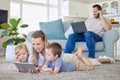 Caucasian mother using a digital tablet with her son and daughter while their father works on a laptop and talks on a Royalty Free Stock Photo