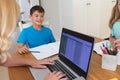 Caucasian mother using laptop and doing homework with her daughter and son smiling in kitchen Royalty Free Stock Photo