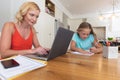 Caucasian mother using laptop and her daughter doing homework smiling at home Royalty Free Stock Photo