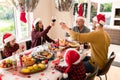 Caucasian multi generation family wearing santa hats having christmas meal, making toast Royalty Free Stock Photo