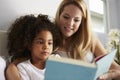 Caucasian mum and black daughter read book in bed, close-up Royalty Free Stock Photo