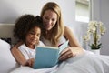 Caucasian mum and black daughter read a book together in bed Royalty Free Stock Photo