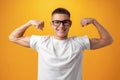 Caucasian muscular teenager boy shows his strength against yellow background