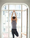 Sporty man practicing yoga in white room with big window. tree pose