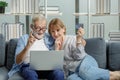 Caucasian old senior elderly grandparents couple sitting cuddling hugging together on sofa in living room at home using credit Royalty Free Stock Photo