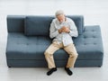 Caucasian old senior elderly gray hair and bearded man lying down close eyes on sofa in living room at home alone holding hands on Royalty Free Stock Photo