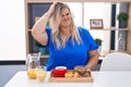 Caucasian plus size woman eating breakfast at home confuse and wonder about question