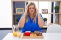 Caucasian plus size woman eating breakfast at home with hand on head for pain in head because stress