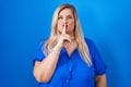 Caucasian plus size woman standing over blue background asking to be quiet with finger on lips