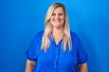 Caucasian plus size woman standing over blue background with a happy and cool smile on face