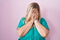 Caucasian plus size woman standing over pink background with sad expression covering face with hands while crying