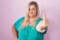 Caucasian plus size woman standing over pink background showing middle finger, impolite and rude fuck off expression