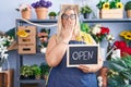 Caucasian plus size woman working at florist holding open sign covering mouth with hand, shocked and afraid for mistake