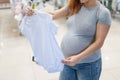 Caucasian pregnant woman chooses baby clothes in a store. Faceless expectant mother in the 3rd trimester.