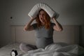 Caucasian pregnant woman sits in bed, holds a pillow on her head and screams. Insomnia. Royalty Free Stock Photo