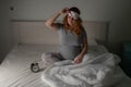 Caucasian pregnant woman sits in bed and looks at the alarm clock. Insomnia. Royalty Free Stock Photo