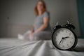 Caucasian pregnant woman sits on the bed and suffers from insomnia. Alarm clock in the foreground. Royalty Free Stock Photo