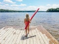 Caucasian preschool blonde girl in pink swimsuit standing on wooden lake river dock with pool noodle on summer day Royalty Free Stock Photo