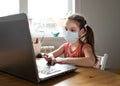 Caucasian preteen girl with medical mask concentrated on her task with laptop. Concept of distance learning in isolation while