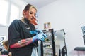 Caucasian pretty tattoo master girl with gloves working in her tattoo studio, medium closeup