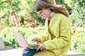 Caucasian pretty young girl, dressed in a yellow jacket, a white sweater, working with the laptop sitting on a park bench Royalty Free Stock Photo