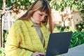 Caucasian pretty young girl, dressed in a yellow jacket, a white sweater, working with the laptop sitting on a park bench Royalty Free Stock Photo