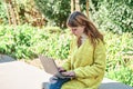 Caucasian pretty young girl, dressed in a yellow jacket, a white sweater, working with the laptop sitting on a park bench Royalty Free Stock Photo