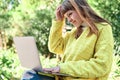 Caucasian pretty young girl, dressed in a yellow jacket, a white sweater, working with the laptop sitting on a park bench Royalty Free Stock Photo