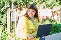 Caucasian pretty young girl, dressed in a yellow jacket, a white sweater, working with the laptop sitting on a park bench Royalty Free Stock Photo