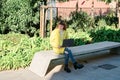 Caucasian pretty young girl, dressed in a yellow jacket, a white sweater, working with the laptop sitting on a park bench Royalty Free Stock Photo