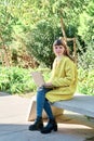 Caucasian pretty young girl, dressed in a yellow jacket, a white sweater, working with the laptop sitting on a park bench Royalty Free Stock Photo