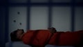 Caucasian prisoner lying and thinking on plank-bed in cell serving life sentence