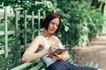 Caucasian red-haired girl sits in the summer in the park on a bench and writes in a notebook Royalty Free Stock Photo