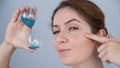 Caucasian red-haired woman holds an hourglass and examines the wrinkles around her eyes. Aging concept.